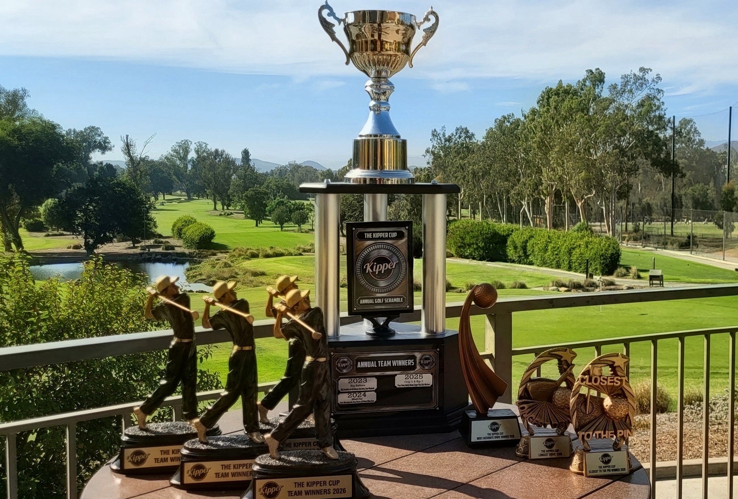 The Kipper Cup perpetual trophy alongside the 2026 Team Winners, Longest Drive, Most Accurate Drive, and Closest to the Pin trophies, displayed at Los Robles Greens