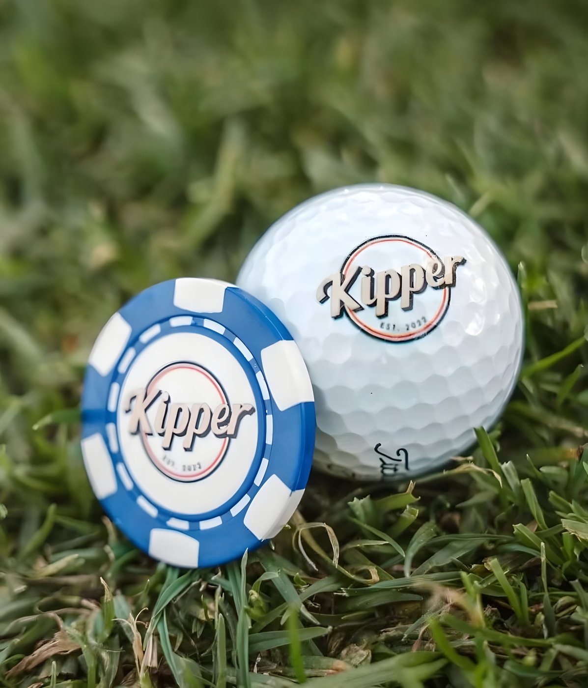 A Kipper-branded golf ball and ball marker resting in the grass